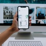 Person uses a smartphone in front of a computer screen displaying stock photos, showcasing modern technology use.